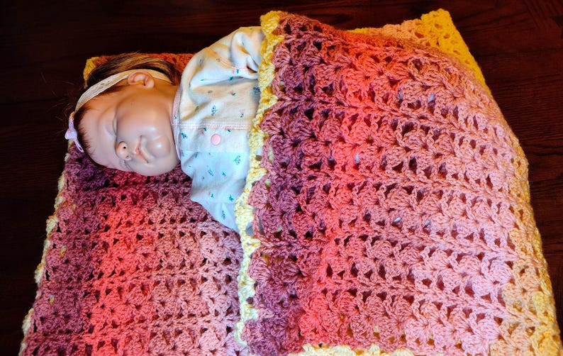 The doll is laying on it's side on a multi-colored striped blanked facing you and the bottom of the blanket covers the bottom of the baby doll.