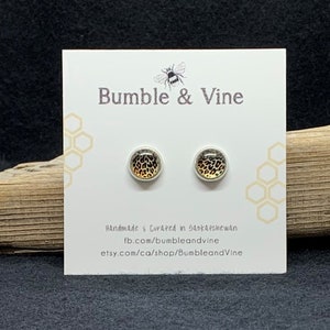 May include: A pair of small, round stud earrings with a leopard print design. The earrings are on a white card with the text "Bumble & Vine" and information about the shop.