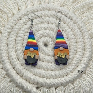May include: A pair of rainbow gnome earrings with a pot of gold. The gnomes are wearing purple trousers and have orange beards. The earrings are silver and have a hook fastening.