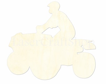 May include: A light-colored wooden cutout of a person riding an ATV. The rider is wearing a helmet and is seated on the four-wheeled vehicle. The ATV has large, rounded tires. The cutout is on a white background.