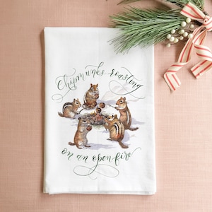 May include: White kitchen towel with a whimsical illustration of chipmunks roasting around a campfire. The text reads "Chipmunks roasting on an open fire."