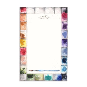 May include: A watercolor notepad with a paint palette border and the word "notes" at the top. A paintbrush is lying on the notepad.