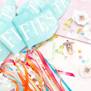 Puede incluir: Un conjunto de decoraciones de fiesta fiesta azules y blancas con la palabra "FIESTA" impresa en las banderas. Las decoraciones incluyen serpentinas, banderas y una peque&ntilde;a figura de un perro con un sombrero.