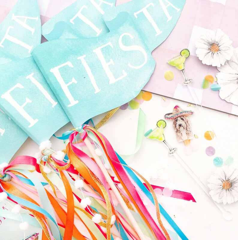 Puede incluir: Un conjunto de decoraciones de fiesta fiesta azules y blancas con la palabra "FIESTA" impresa en las banderas. Las decoraciones incluyen serpentinas, banderas y una peque&ntilde;a figura de un perro con un sombrero.