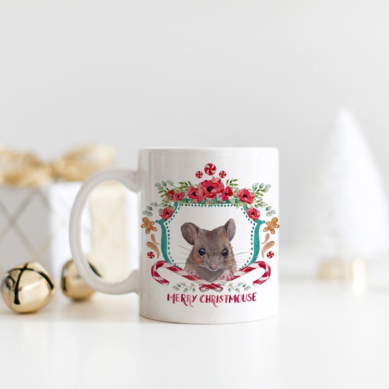 May include: White ceramic mug with a festive design featuring a mouse peeking out of a wreath of red flowers and candy canes. The text "Merry Christmouse" is printed on the mug.