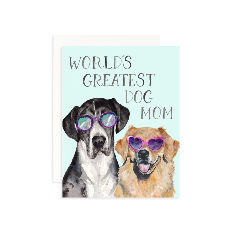 May include: Greeting card with a light blue background featuring two dogs wearing sunglasses. The text "WORLD'S GREATEST DOG MOM" is printed above the dogs. One dog is black and white, the other is golden.
