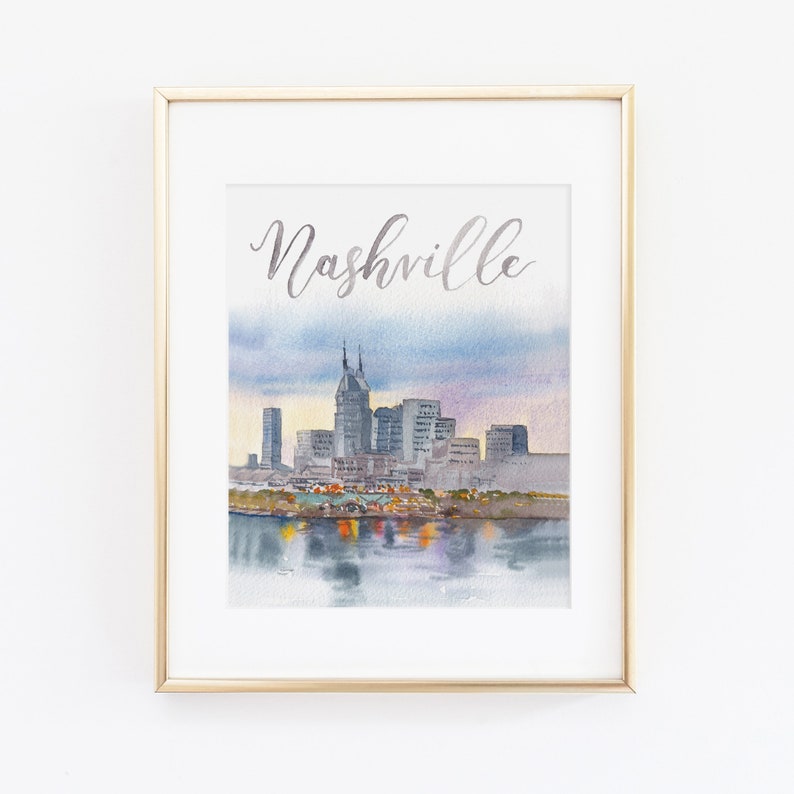 May include: A watercolour painting of the Nashville skyline with the word "Nashville" written in silver script at the top. The skyline is depicted in shades of grey and blue, with a reflection of the city in the water below.