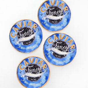 May include: Four round blue and gold caviar labels with the word "CAVIAR" in gold lettering. Each label features a fish illustration and the word "Fancy" in cursive. The text "EGG-SQUISITE" is also visible.