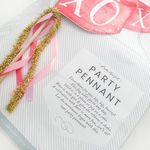 Puede incluir: Una tarjeta blanca con el texto "Party Pennant" y una descripci&oacute;n de c&oacute;mo usar el bander&iacute;n. La tarjeta est&aacute; sobre un fondo a rayas con una cinta rosa y dorada.
