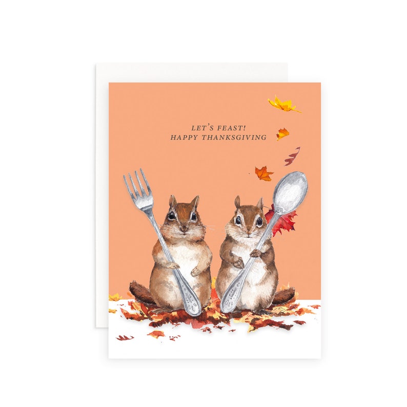 May include: Thanksgiving card with two chipmunks holding a fork and spoon. The card has an orange background with the text "LET'S FEAST! HAPPY THANKSGIVING" and falling leaves. The chipmunks are surrounded by autumn leaves.