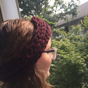May include: A close-up of a person wearing a maroon crocheted headband. The headband is thick and has a textured pattern. The person is looking out of a window.