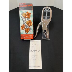 May include: A vintage Cracker Jack nutcracker set. The set includes a chrome-plated nutcracker, a box with squirrel illustrations, and an instruction sheet. The box reads "Cracks Nuts Crab & Lobster Claws Crushes Ice Cubes."