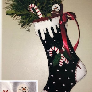 May include: A black felt Christmas stocking with white polka dots and a white felt cuff. The stocking is decorated with a green felt holly sprig, red and white candy canes, and a small felt snowman. The stocking is filled with green pine sprigs and a red and white candy cane.