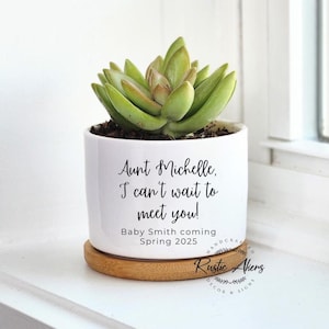 May include: White ceramic planter with a succulent plant. The planter has a message that reads "Aunt Michelle, I can't wait to meet you! Baby Smith coming Spring 2025".