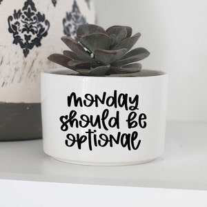 May include: White ceramic planter with a succulent plant and the text "Monday should be optional" in black lettering.