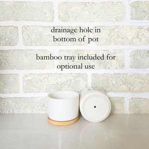 May include: White ceramic plant pot with a bamboo tray. The pot has a drainage hole in the base. The image text reads "drainage hole in bottom of pot" and "bamboo tray included for optional use".