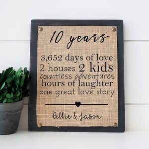 May include: A black framed burlap sign with the text "10 years", "3,652 days of love", "2 houses 2 kids", "countless adventures", "hours of laughter", "one great love story", and "Allie & Jason".