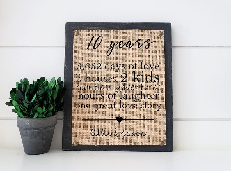 May include: A black framed burlap sign with the text "10 years", "3,652 days of love", "2 houses 2 kids", "countless adventures", "hours of laughter", "one great love story", and "Allie & Jason".