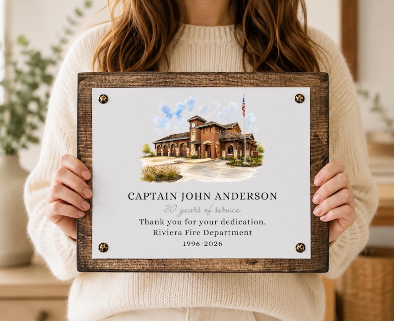 Puede incluir: Una placa rectangular de madera con un panel central blanco que presenta una ilustraci&oacute;n en acuarela de una estaci&oacute;n de bomberos y una bandera estadounidense. El texto dice: CAPTAIN JOHN ANDERSON, 30 years of service, Thank you for your dedication, Riviera Fire Department, 1996-2026.