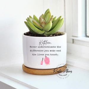 May include: White ceramic planter with a succulent plant and the text "Kathleen, Never underestimate the difference you make and the lives you touch."  The planter has a wooden base and a pink nail polish design.