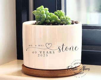 Può includere: Vaso in ceramica bianca con base in bambù. Il vaso ha un testo nero che recita "Mr. & Mrs. stone 40 Years 2025". Il testo è in un font corsivo con un simbolo di cuore. Il vaso è riempito con una piccola pianta succulenta.