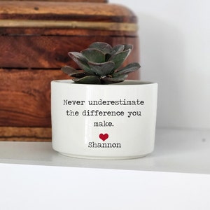 May include: White ceramic planter with a succulent plant. The planter has the text "Never underestimate the difference you make." and "Shannon" with a red heart.