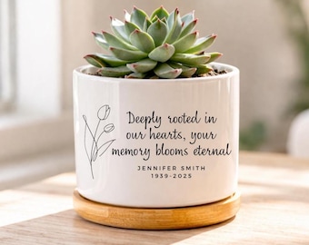 May include: A white ceramic planter with a succulent plant, on a wooden saucer. The planter features a floral illustration and the text "Deeply rooted in our hearts, your memory blooms eternal" with a name and dates.