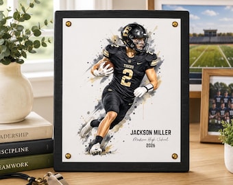 May include: A rectangular black wooden frame holding a white print of a football player in a black uniform with the number 2, featuring watercolor-style splashes. The text reads JACKSON MILLER, Madison High School, and 2026, secured by four gold screws.