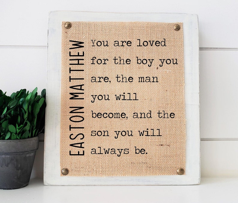 May include: A white wooden sign with a burlap background and the text "EASTON MATTHEW You are loved for the boy you are, the man you will become, and the son you will always be."