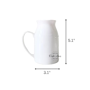 May include: A white ceramic pitcher with a handle, measuring 5.1 inches tall and 3.1 inches wide. The pitcher has a ruffled top and a curved handle. The words "Rustic Akers" are printed on the side.