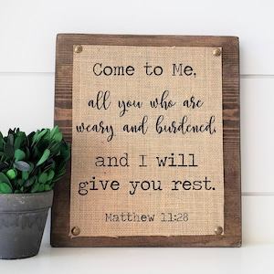 May include: A wooden sign with a burlap background featuring the quote "Come to Me, all you who are weary and burdened and I will give you rest. Matthew 11:28".