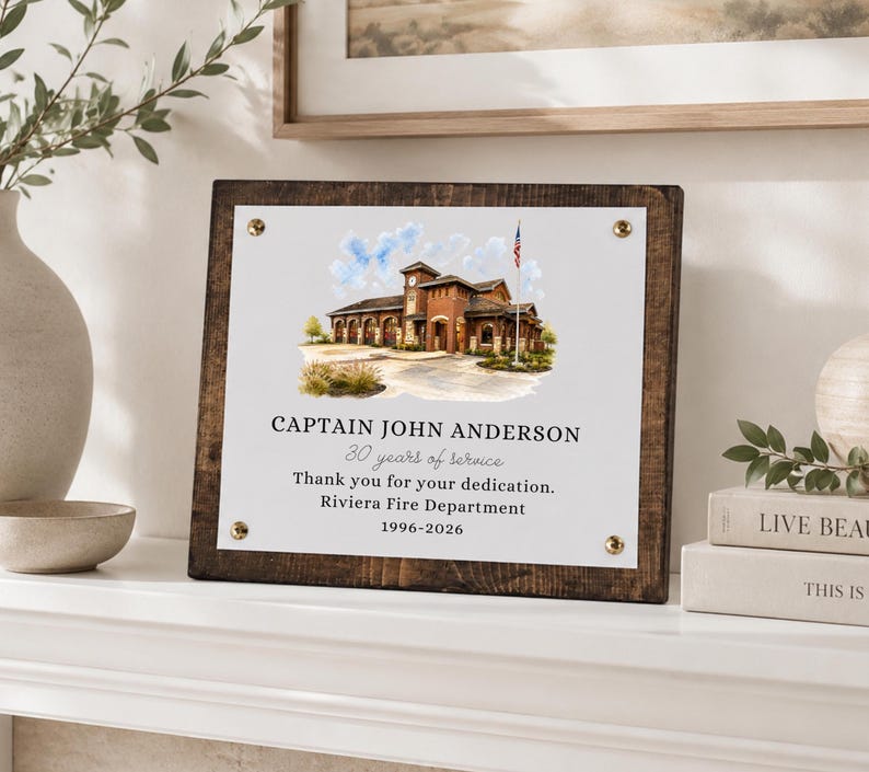 Puede incluir: Una placa rectangular de madera con un panel central blanco que presenta una ilustraci&oacute;n en acuarela de una estaci&oacute;n de bomberos y el texto: CAPTAIN JOHN ANDERSON, 30 years of service, Thank you for your dedication, Riviera Fire Department, 1996-2026.