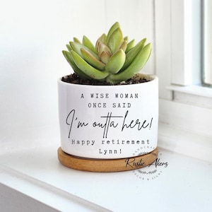 May include: White ceramic planter with a succulent plant and the text "A wise woman once said I'm outta here! Happy retirement Lynn!"  The planter has a bamboo base and a Rustic Akens logo.