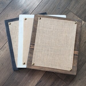 May include: Three wooden frames with burlap inserts. The frames are stacked on top of each other. The top frame is brown, the middle frame is white, and the bottom frame is black.
