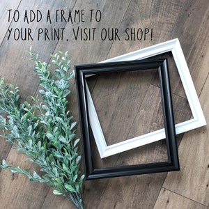 May include: Two picture frames, one black and one white, are lying on a wood floor. The frames are overlapping. The text "To add a frame to your print, visit our shop!" is written on the floor above the frames.