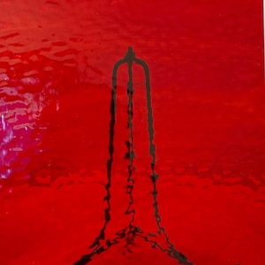 May include: Abstract artwork featuring a bold red background with a dark, vertical, stylized shape resembling a tower or structure. The shape has three vertical lines connected at the top.