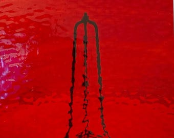 May include: Abstract art piece with a vibrant red backdrop and a dark, vertical, stylized shape, possibly a tower or structure. The shape has three vertical lines joined at the top.