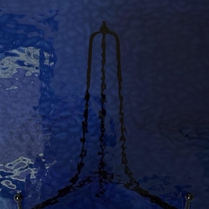 May include: A dark blue, abstract image with a textured surface. A black, stylized, elongated shape is centered, resembling a decorative element or stand. The background transitions from lighter to darker shades of blue.
