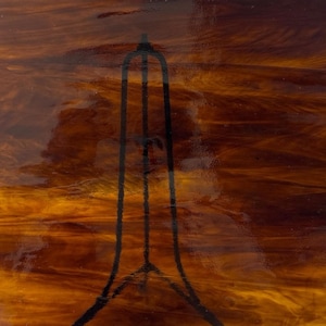 May include: Abstract stained glass panel with a warm color palette of amber, brown, and gold. A black, stylized architectural design is overlaid on the glass, creating a striking contrast. The glass has a glossy finish.