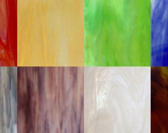 May include: A collection of eight glass tiles in various colors and patterns, including red, yellow, green, blue, gray, brown, white, and brown. The tiles have a marbled or swirled appearance.