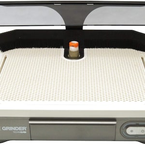 May include: A glass grinder with a white perforated work surface, a black splash guard, and a clear shield. The base is gray with the text "THE GRINDER TECH-GLASS". The grinder has an orange and white grinding head.