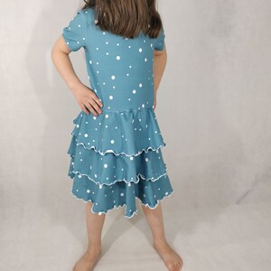 Puede incluir: Un vestido azul turquesa con lunares blancos y una falda de volantes de varios niveles.