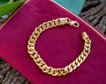 May include: A gold-toned curb chain bracelet featuring interlocking flat, oval links and a secure lobster claw clasp. The bracelet is polished to a high shine, reflecting light across its smooth, metallic surface. The text Sterling Style Shop is visible.