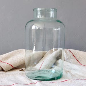 May include: A large, clear glass jar with a wide mouth and a slightly green tint. The jar is sitting on a white and red striped fabric.