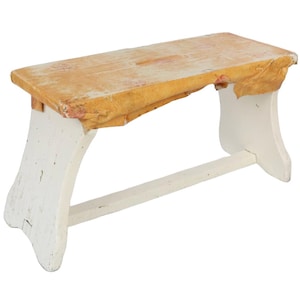 Può includere: Uno sgabello in legno bianco con un piano di colore marrone chiaro. Lo sgabello ha un design semplice con un unico traverso che collega le gambe.