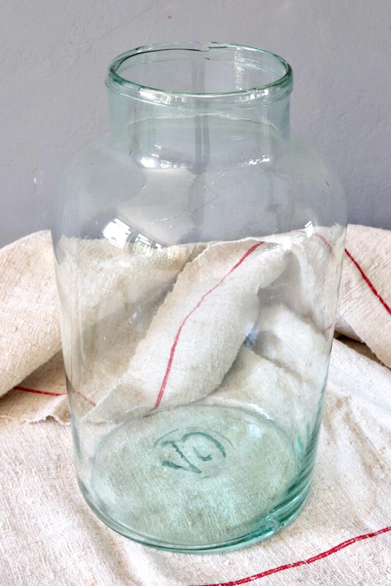 May include: A large, clear glass jar with a green tint. The jar has a wide mouth and a rounded bottom. The jar is sitting on a white and red striped cloth.