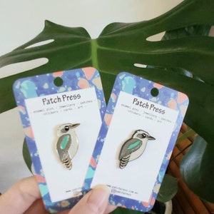 May include: Two cards with a blue, pink and white abstract pattern. Each card features a gold enamel pin of a kookaburra bird with a turquoise blue chest. The text on the cards reads "Patch Press enamel pins - jewellery - patches - stickers - cards - art".