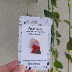 May include: A white card with a pink and grey enamel pin of a cockatoo. The card says "Patch Press" and "enamel pins - iron on patches - stickers - knapsacks". The card also has the website "www.patchpress.com.au" and the Instagram handle "@patchpress".
