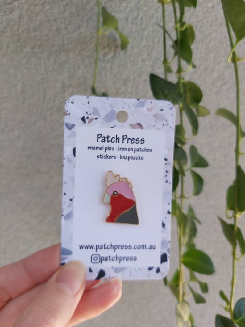 May include: A white card with a pink and grey enamel pin of a cockatoo. The card says "Patch Press" and "enamel pins - iron on patches - stickers - knapsacks". The card also has the website "www.patchpress.com.au" and the Instagram handle "@patchpress".