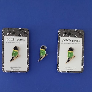 May include: Two black and green bird enamel pins on white cards with the text "patch press" and website information.